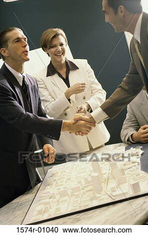 Stock Image - Business executives shaking hands at a presentation. Fotosearch