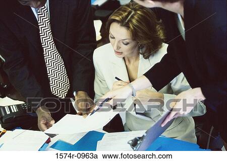 Stock Image - Businesswoman looking at documents in her colleagues hands. Fotosearch