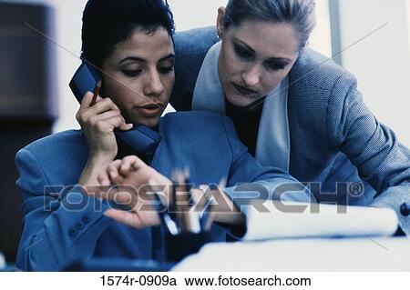 Businesswoman looking at her wristwatch while talking on a landline phone View Large Photo Image Stock Image - Businesswoman looking at her wristwatch while talking on a landline phone. Fotosearch