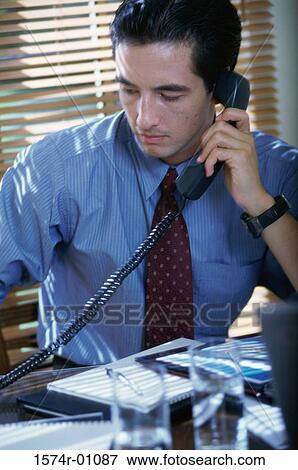 Close-up of a young businessman using the landline telephone at his desk View Large Photo Image Stock Photo - Close-up of a young businessman using the landline telephone at his desk. Fotosearch
