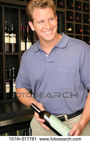Close-up of a mid adult man holding a wine bottle in a liquor store View Large Photo Image Stock Image - Close-up of a mid adult man holding a wine bottle in a liquor store. Fotosearch