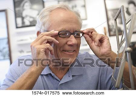 Stock Photography - Close-up of a senior man trying on eyeglasses in a store. Fotosearch