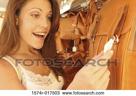 Close-up of a young woman looking at the price tag on a bag in a store View Large Photo Image Stock Image - Close-up of a young woman looking at the price tag on a bag in a store. Fotosearch