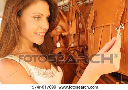 Stock Photo - Close-up of a young woman looking at the price tag on a bag. Fotosearch