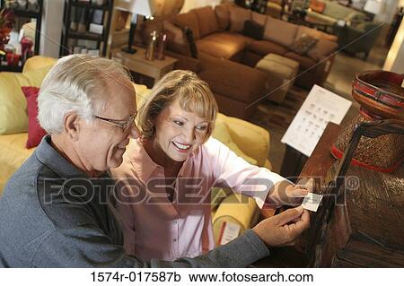 Stock Image - High angle view of a senior couple looking at a price tag in a furniture store. Fotosearch