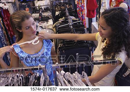 Stock Photo - High angle view of a young woman selecting a top for her friend in a clothing store. Fotosearch