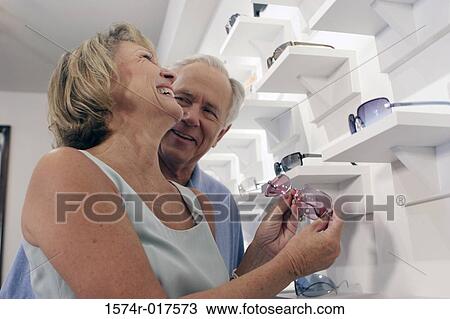 Stock Image - Low angle view of a senior couple selecting sunglasses in a store. Fotosearch