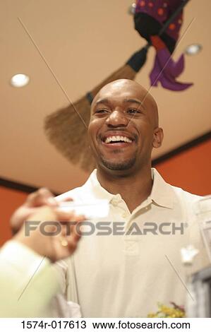 Stock Image - Low angle view of a young man handing a credit card to a sales clerk. Fotosearch