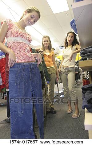 Low angle view of a young woman holding a pair of jeans in front of her friends in a clothing store View Large Photo Image Stock Photo - Low angle view of a young woman holding a pair of jeans in front of her friends in a clothing store. Fotosearch