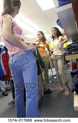 Stock Photo - Low angle view of a young woman trying on a pair of jeans in a clothing store. Fotosearch