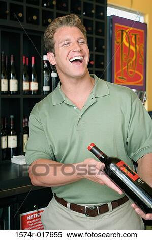 Mid adult man holding a wine bottle in a liquor store View Large Photo Image Stock Photography - Mid adult man holding a wine bottle in a liquor store. Fotosearch