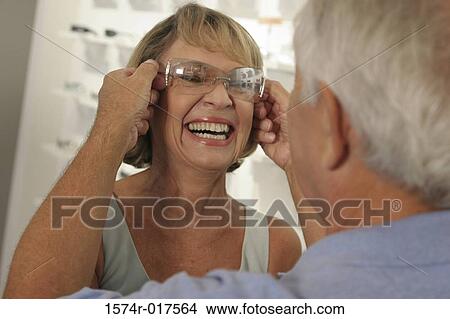 Picture - Rear view of a senior man putting sunglasses on a senior woman in a store. Fotosearch