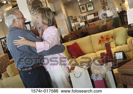 Stock Photograph - Side profile of a senior couple dancing in a furniture store. Fotosearch