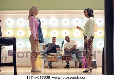 Stock Photo - Side profile of a young woman showing her new dress to her friends in a store. Fotosearch