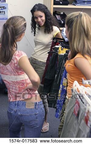 Stock Image - Three young women selecting clothes in a clothing store. Fotosearch