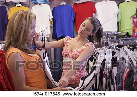 Stock Photography - Young woman selecting a tank top for her friend in a clothing store. Fotosearch
