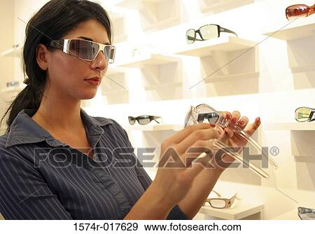 Young woman trying on sunglasses in a store View Large Photo Image Stock Photo - Young woman trying on sunglasses in a store. Fotosearch