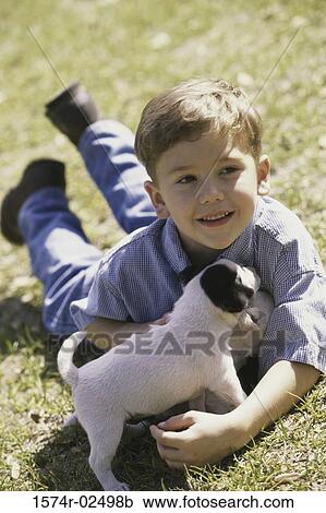 Boy lying on a lawn holding a puppy View Large Photo Image Stock Image - Boy lying on a lawn holding a puppy. Fotosearch
