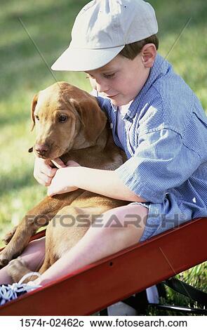 Stock Image - Boy sitting in a toy wagon holding his dog. Fotosearch