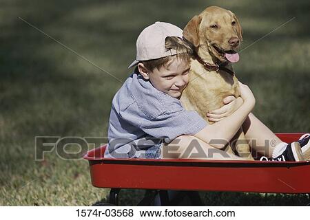 Boy sitting in a toy wagon holding his dog View Large Photo Image Stock Photo - Boy sitting in a toy wagon holding his dog. Fotosearch
