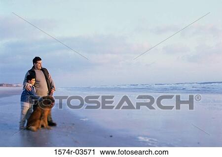 Father and his son standing with their dog on the beach View Large Photo Image Stock Image - Father and his son standing with their dog on the beach. Fotosearch