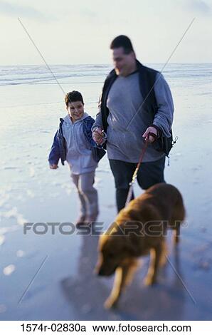 Stock Image - Father and his son walking with their dog on the beach. Fotosearch