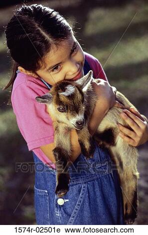 Stock Image - High angle view of a girl holding a kid goat in her arms. Fotosearch