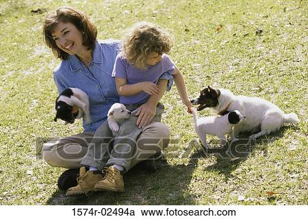 Stock Image - High angle view of a mother and her daughter playing with puppies. Fotosearch