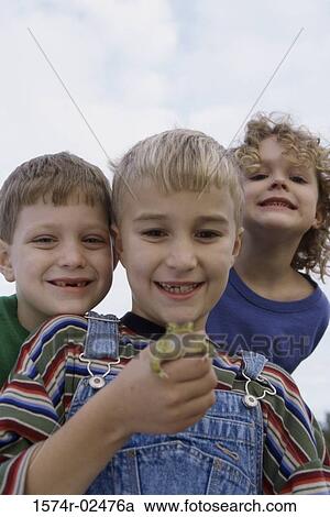 Stock Image - Low angle view of a boy standing with his friends holding a frog. Fotosearch