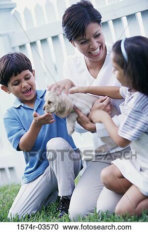 Stock Image - Mother with her son and daughter petting a puppy. Fotosearch