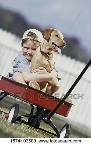 Stock Photo - Portrait of boy sitting in a toy wagon holding his dog. Fotosearch