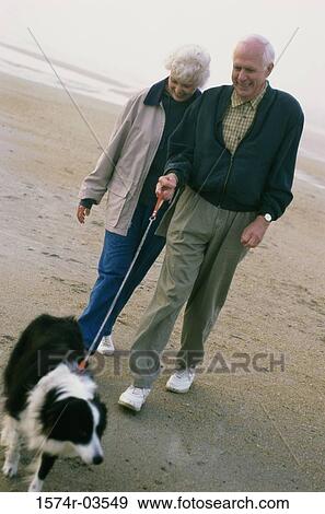 Stock Photo - Senior couple walking with their dog on the beach. Fotosearch