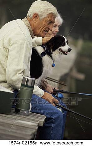 Stock Image - Side profile of a senior couple fishing on a pier with their dog. Fotosearch