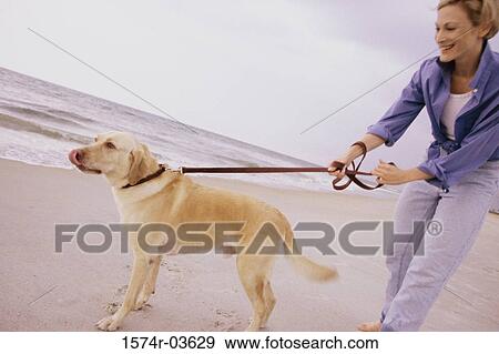 Stock Photo - Young woman holding her dog on the beach. Fotosearch