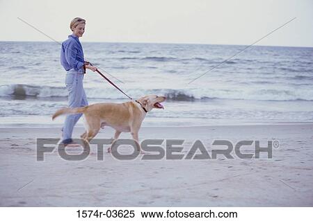 Stock Photography - Young woman walking with her dog on the beach. Fotosearch