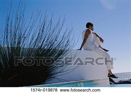 Low angle view of a young man sitting on a wall View Large Photo Image Stock Photo - Low angle view of a young man sitting on a wall. Fotosearch