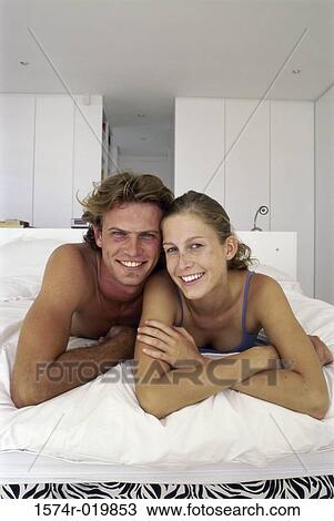 Portrait of a young couple lying on a bed View Large Photo Image Stock Image - Portrait of a young couple lying on a bed. Fotosearch
