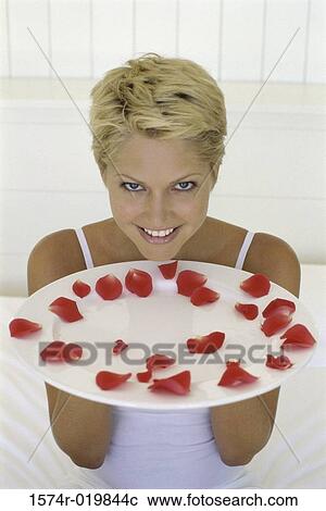 Stock Image - Young woman holding a plate with rose petals. Fotosearch