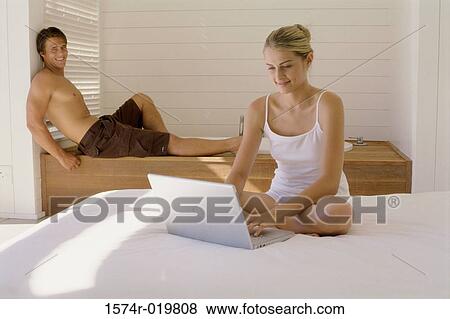 Young woman working on a laptop with a young man sitting behind her View Large Photo Image Stock Photo - Young woman working on a laptop with a young man sitting behind her. Fotosearch