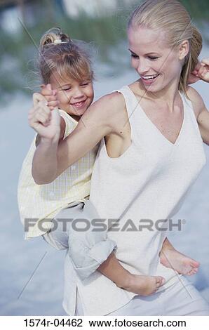 Stock Image - Daughter riding piggyback on her mother on the beach. Fotosearch