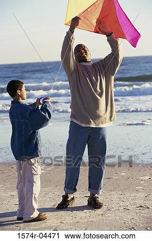 Stock Image - Father and his son flying a kite on the beach. Fotosearch