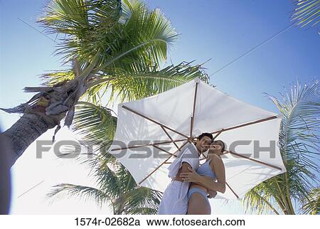 Stock Image - Low angle view of a young couple embracing on the beach. Fotosearch