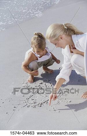 Mother and daughter drawing in the sand on the beach View Large Photo Image Stock Image - Mother and daughter drawing in the sand on the beach. Fotosearch