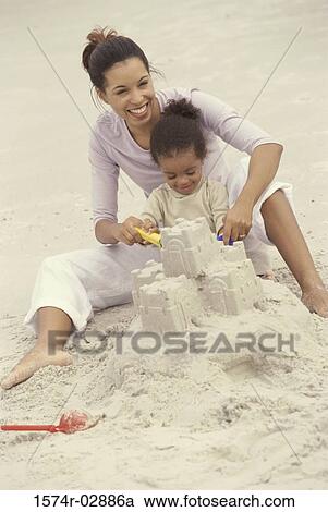 Stock Image - Mother and her daughter making a sand castle on the beach. Fotosearch