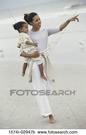 Stock Image - Mother carrying her daughter on the beach. Fotosearch