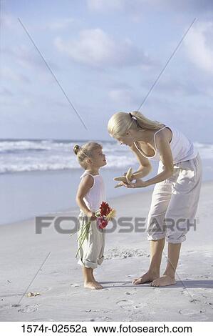Stock Image - Mother showing her daughter a starfish on the beach. Fotosearch