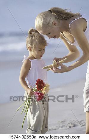 Stock Image - Mother showing her daughter a starfish on the beach. Fotosearch