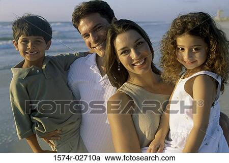 Stock Image - Parents holding their son and daughter on the beach. Fotosearch