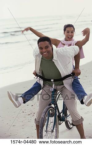 Stock Image - Portrait of a young couple riding a bicycle on the beach. Fotosearch
