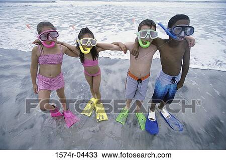 Stock Image - Portrait of two boys and two girls wearing snorkels standing in a row on the beach. Fotosearch